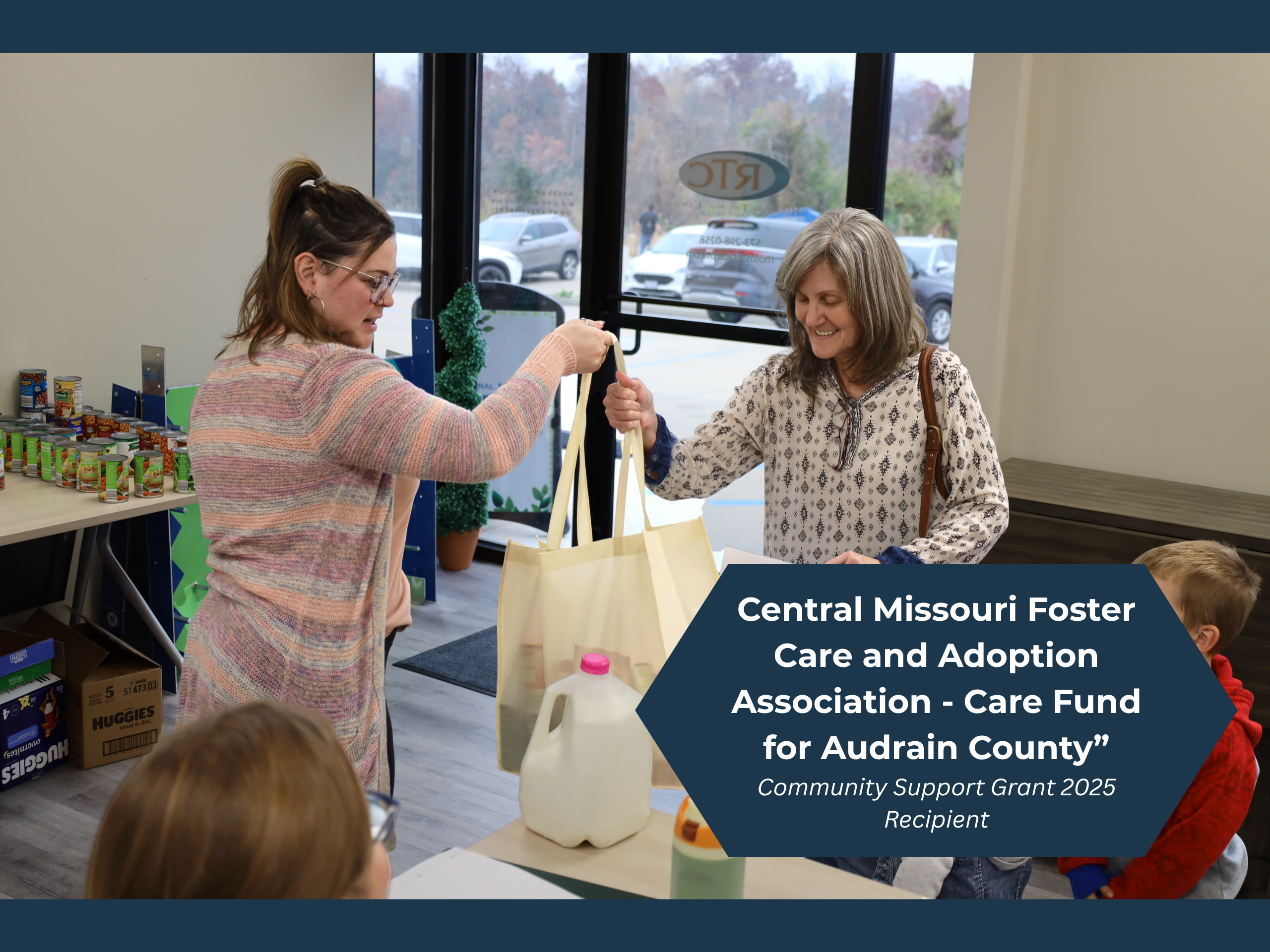 A woman and two children are handed a bag of supplies by a CMFCAA employee, aiding their community.